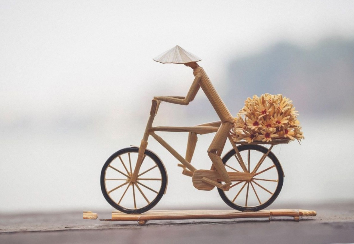 Kleine Bambusfigur auf dem Fahrrad mit Blumenkorb